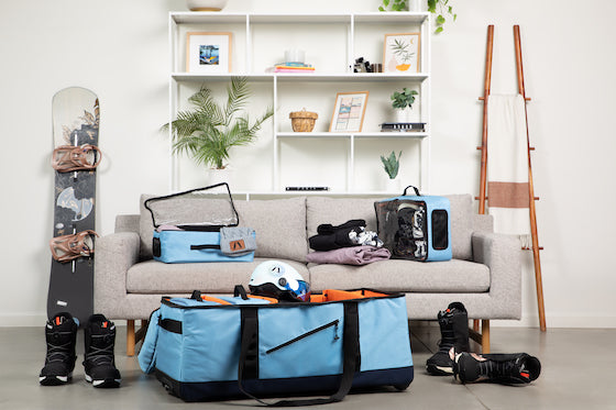 Living room with blue and orange duffel on floor being packed with ski and snowboard gear 